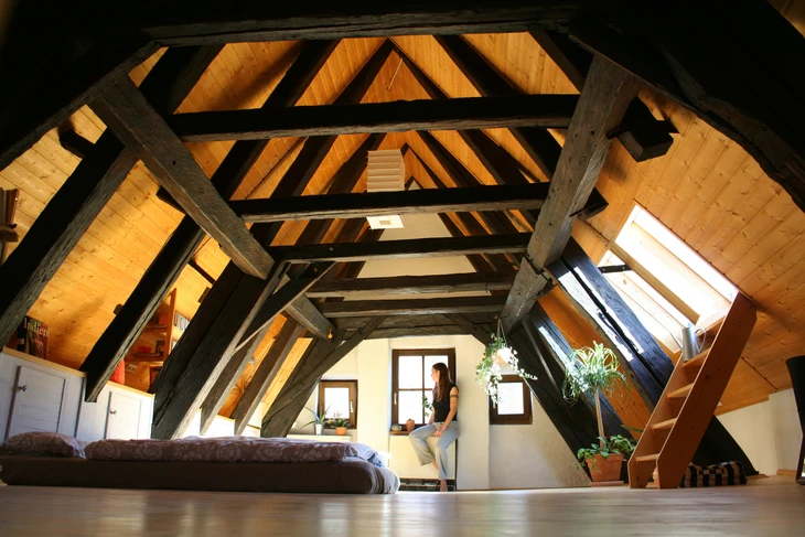 Intérieur mansardé avec charpente apparente en bois, poutres transversales et fermes traditionnelles