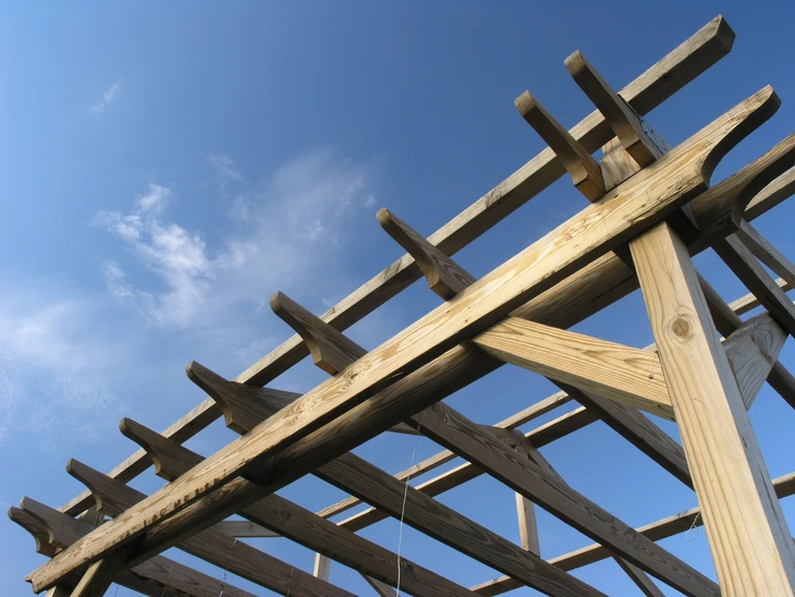 Chantier de construction extérieur avec charpente en bois brut en cours d'assemblage sous ciel bleu nuageux