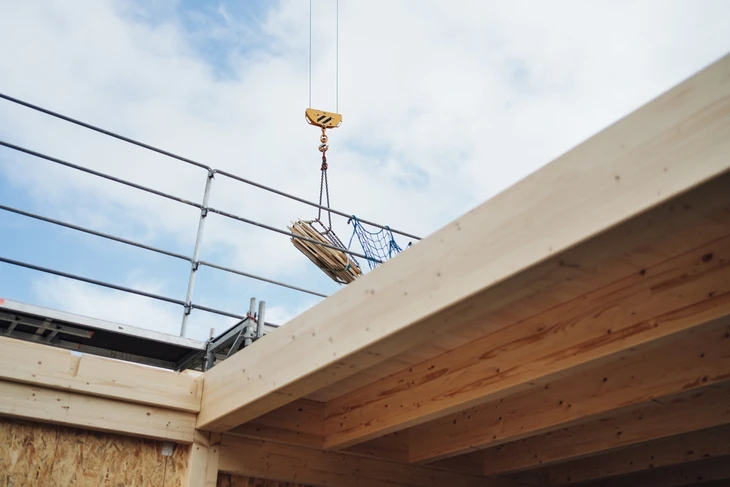 Chantier de construction extérieur avec grue mobile soulevant un paquet de matériaux au-dessus d'une structure en cours d'édification