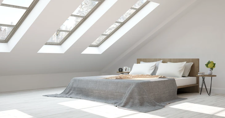 Chambre sous combles aménagée avec lit double plateforme en bois, couverture grise texturée, oreillers blancs
