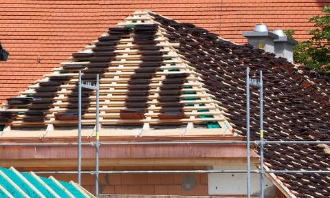 Maison individuelle scandinave à ossature bois avec bardage vertical orange, toiture en tuiles grises et balcon à l'étage