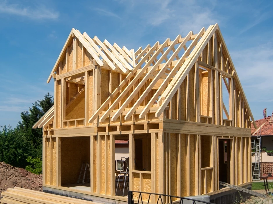 Structure d'ossature bois en cours de construction, deux niveaux, charpente traditionnelle apparente avec fermes de toit triangulées et chevrons