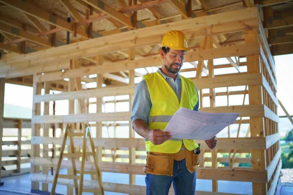 Ouvrier en bâtiment consulte des plans sur chantier de construction à ossature bois