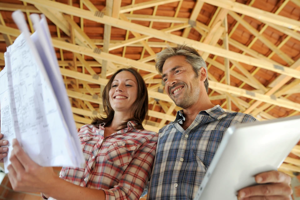 Couple souriant dans maison en construction examine plans architecturaux