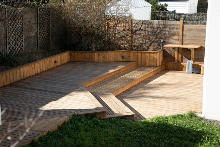 Terrasse extérieure en bois avec banquette intégrée d'angle et marches, située dans jardin résidentiel