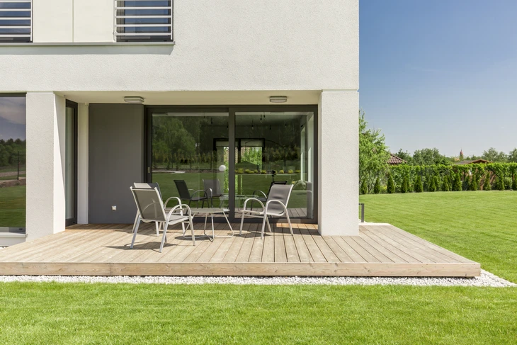 Terrasse extérieure moderne avec mobilier de jardin contemporain, maison à architecture minimaliste avec grandes baies vitrées coulissantes, pelouse entretenue et végétation paysagée