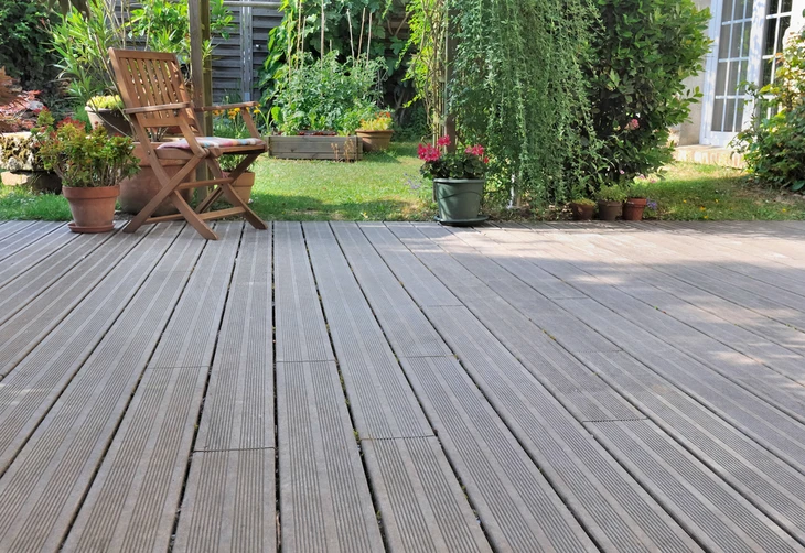 Terrasse extérieure en lames de bois composite grisées avec chaise pliante en teck, pots de fleurs et jardin verdoyant en arrière-plan
