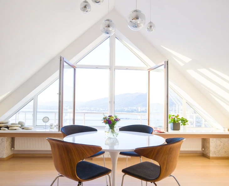 Salle à manger moderne sous combles avec table ronde blanche et chaises design en bois courbé à assises bleues