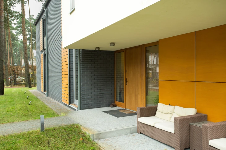Terrasse couverte moderne avec salon de jardin en résine tressée face à une maison contemporaine