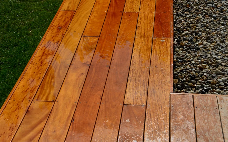 Terrasse extérieure en bois exotique mouillée par la pluie, entourée de gazon vert et graviers décoratifs
