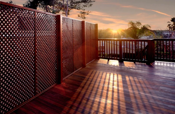 Terrasse extérieure en bois exotique au coucher du soleil avec claustra à treillis diagonal et garde-corps à barreaudage vertical
