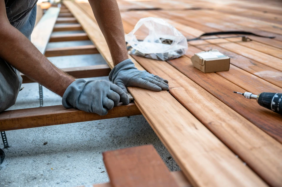 Un travailleur portant des gants aligne soigneusement des planches de bois tout en construisant un pont, avec des outils et des matériaux comme une perceuse et des vis visibles à la surface