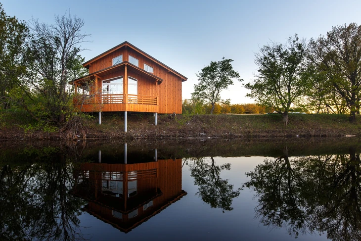 Maison contemporaine en bois sur pilotis située au bord d'un étang, avec terrasse et garde-corps horizontaux