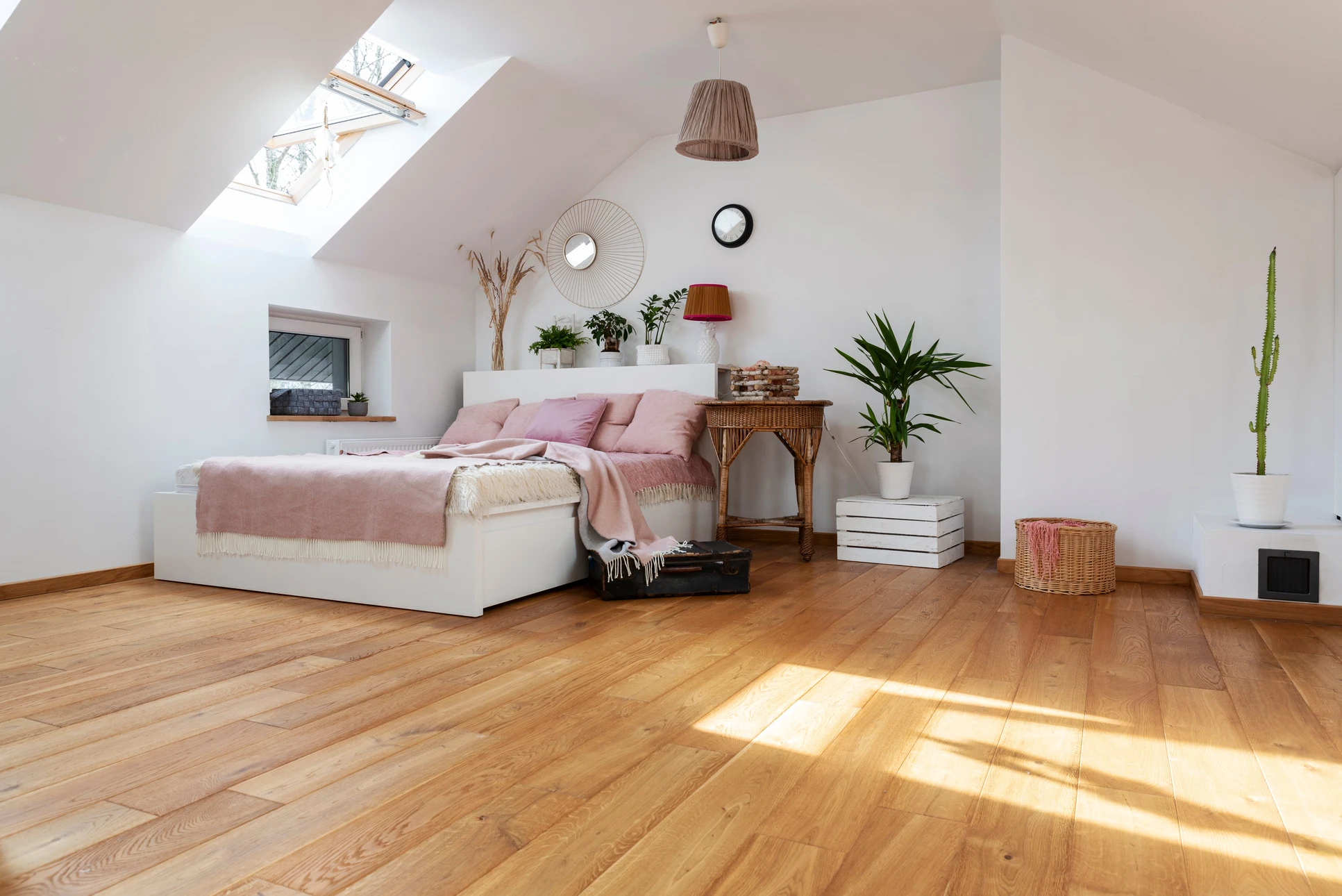 Chambre mansardée moderne avec lit blanc garni de coussins roses et plaid beige