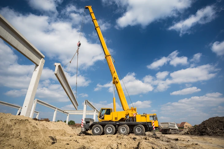 Chantier de construction extérieur avec grue mobile jaune installant des éléments préfabriqués en béton