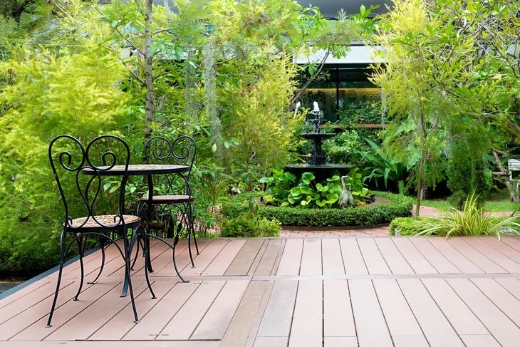Terrasse en bois composite avec salon de jardin en fer forgé noir dans jardin paysager