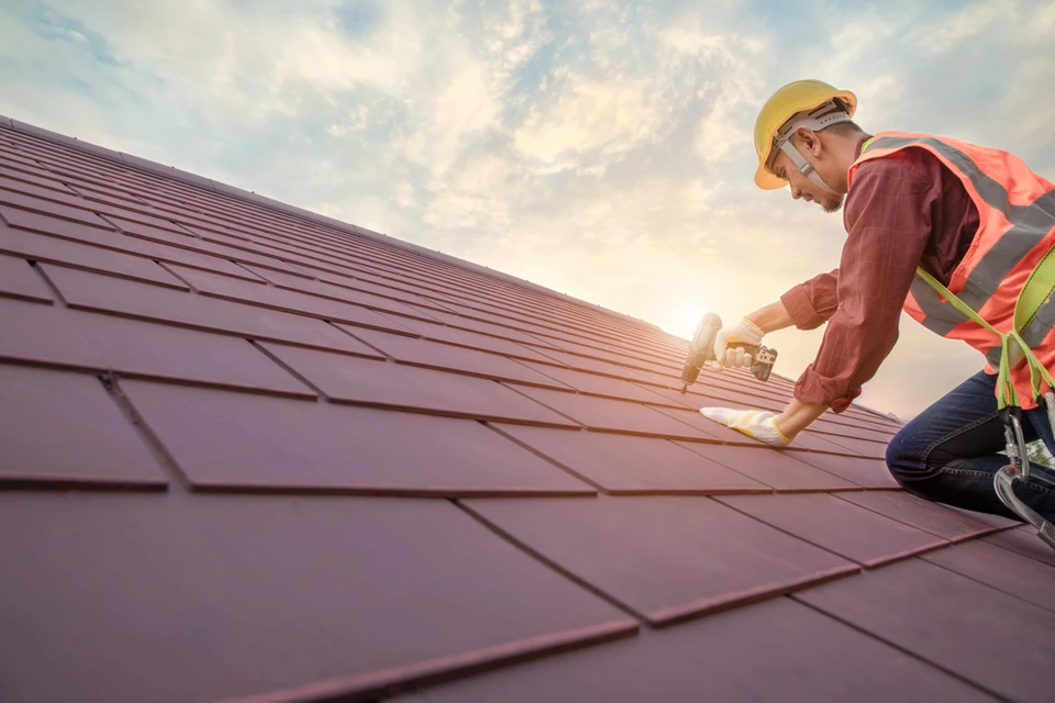 Ouvrier couvreur en équipement de sécurité installant des tuiles photovoltaïques sur toiture résidentielle par temps ensoleillé