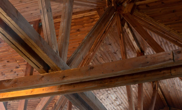 Intérieur d'une charpente en bois, vue en contre-plongée sur l'assemblage de poutres et chevrons