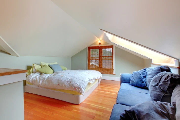 Chambre mansardée moderne avec lit blanc suspendu, canapé bleu, parquet en bois massif